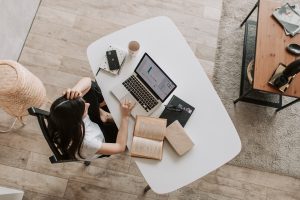 Birds eye view of woman working remotely at desk. Using laptop with notebook beside her.